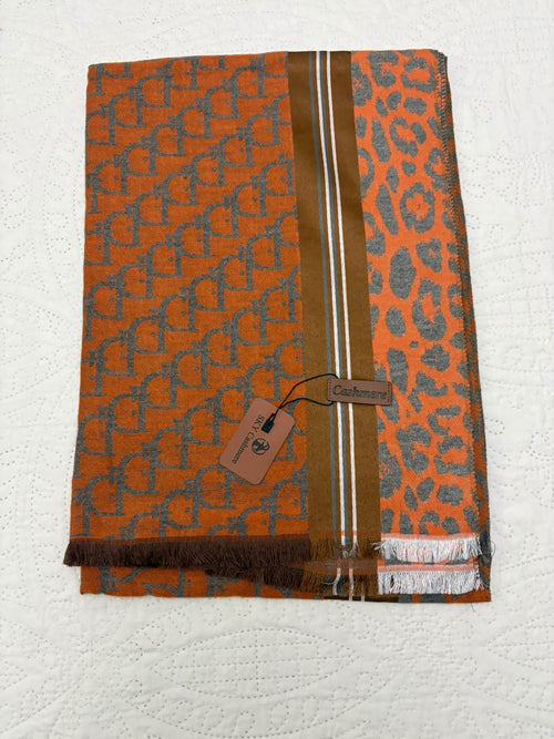 An orange woven scarf with a gray repeating monogram pattern, a leopard print section, and a vertical brown stripe with white lines, laid flat on a white textured background with a brand tag attached.