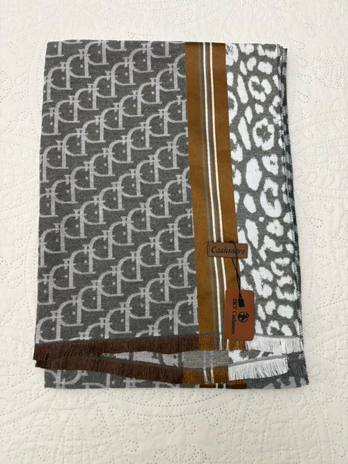 A folded knit scarf featuring a gray and white repeating monogram pattern on one side, a white leopard print on the other, and a central vertical stripe in brown and white. The scarf has fringed edges and a brown leather brand tag reading 'Carmen' with a 'C' logo.