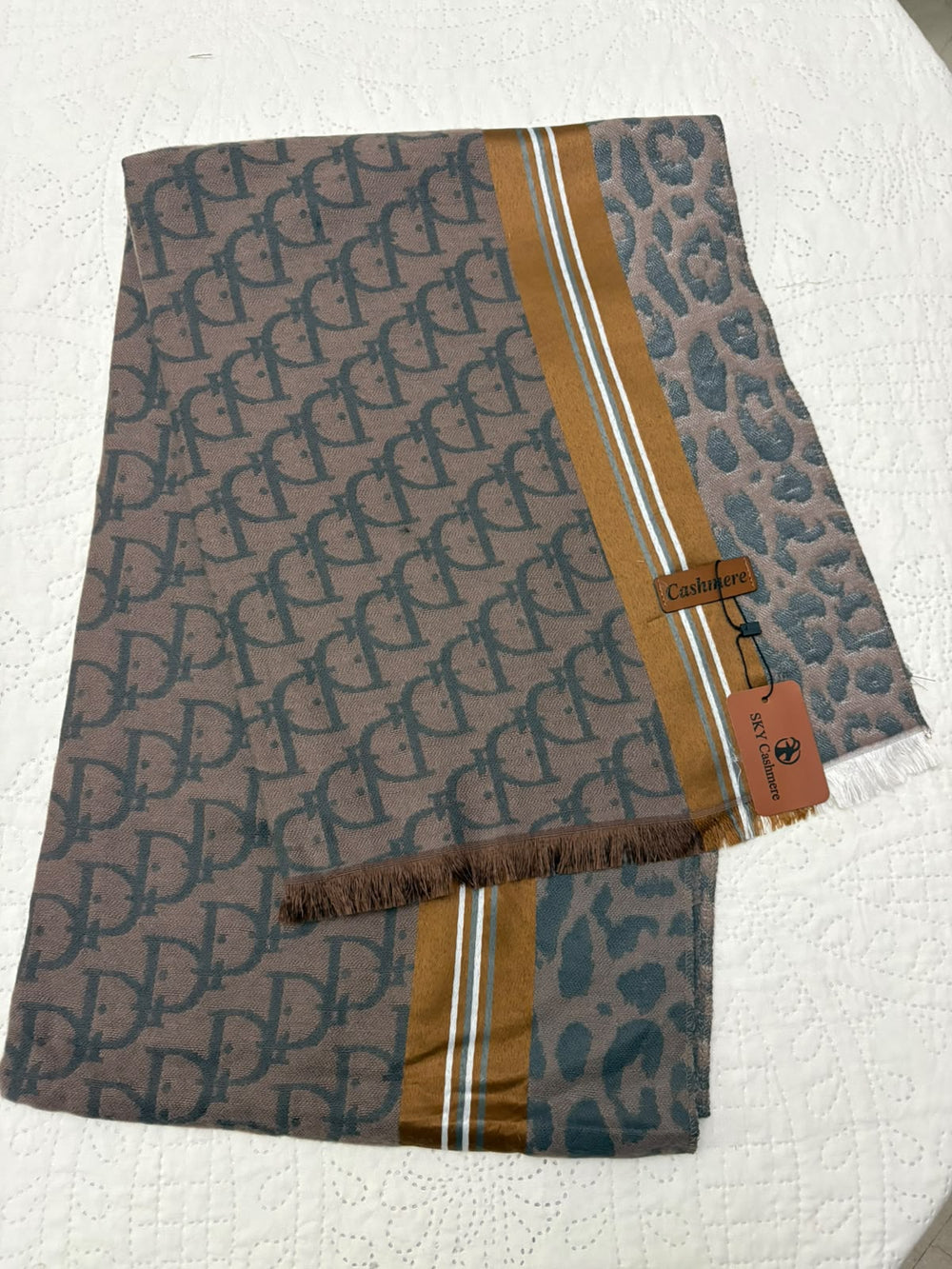 A folded designer scarf featuring a brown and gray interlocking monogram pattern, a leopard print border, and gold and white stripes, with a visible Celine tag.