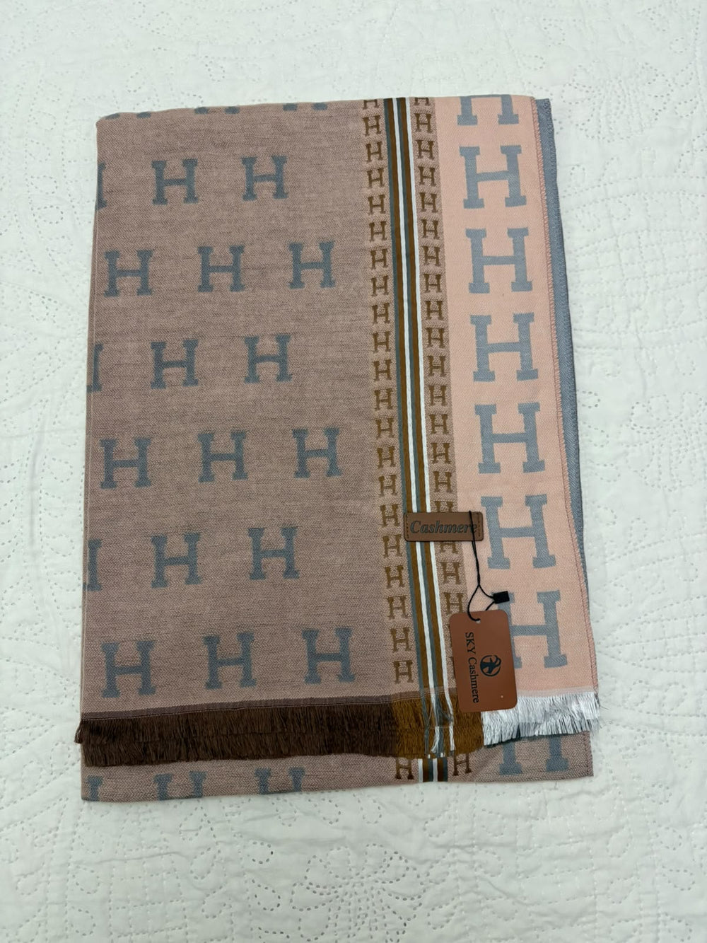 A folded Hermès scarf in a dusty pink and brown colorway, featuring the signature repeating 'H' pattern and a brown leather brand tag.