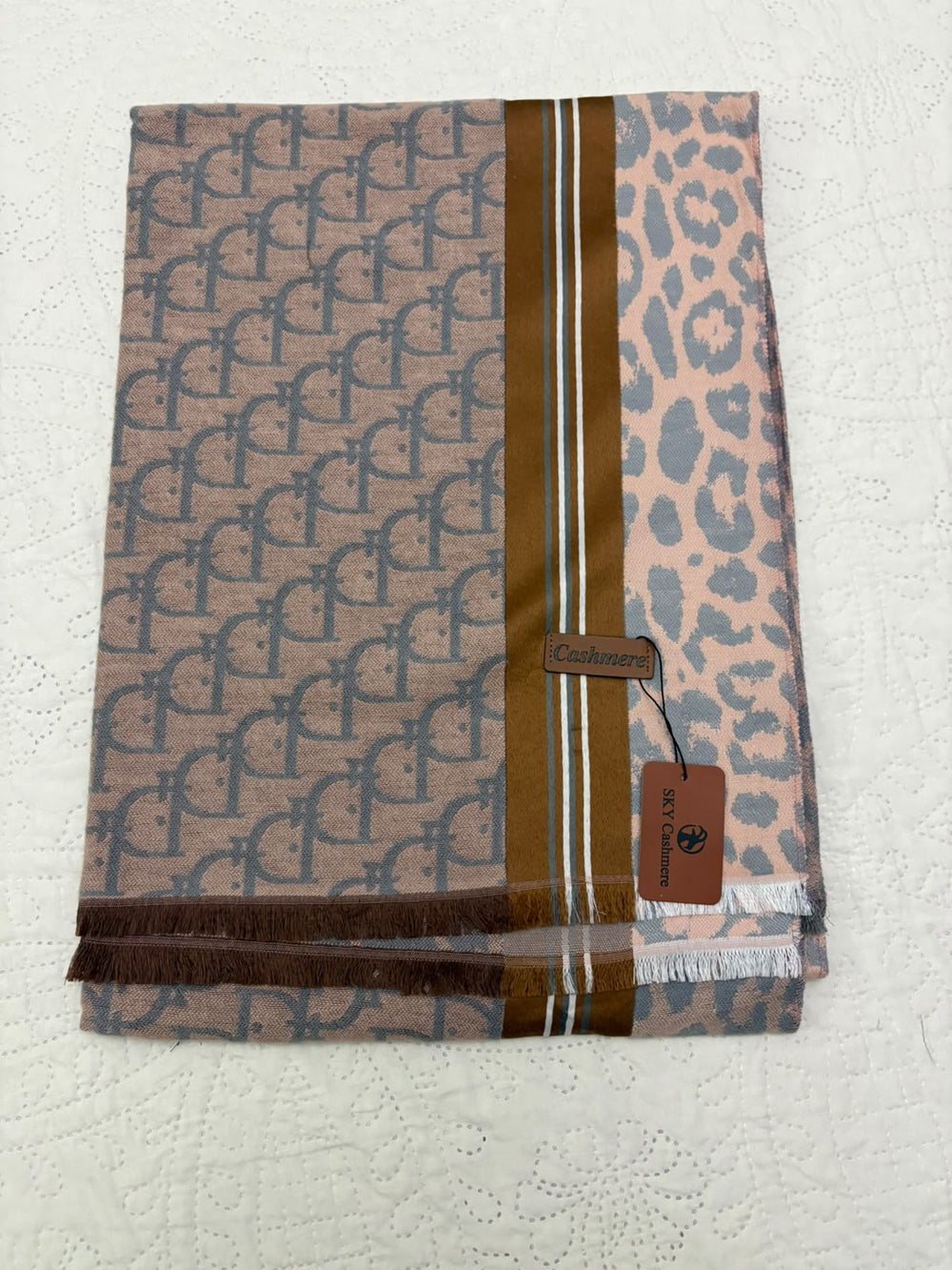 A folded scarf featuring a split design: one side has a brown and beige repeating monogram pattern, and the other side has a pink leopard print. A vertical brown stripe runs down the center with thin white accent lines.