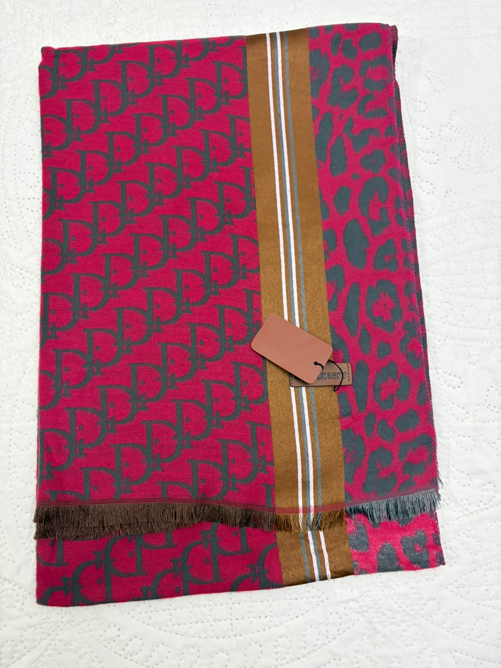 A folded designer scarf featuring a magenta-pink background with dark gray interlocking monogram pattern on one side, a dark gray leopard print on the other, and a central gold stripe with thin white lines. A brown leather hangtag is attached.