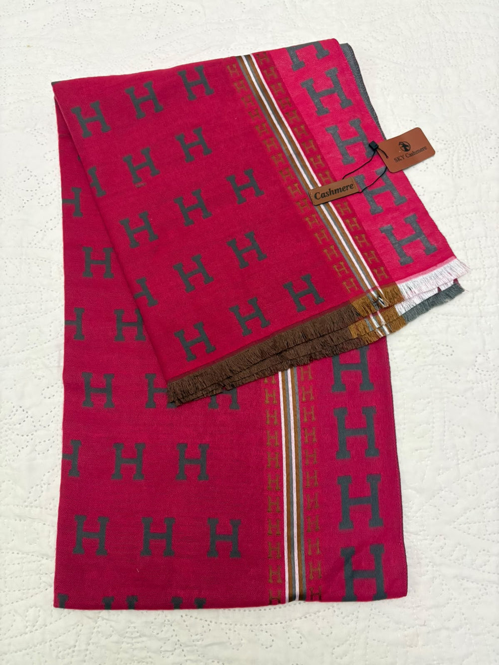 A folded magenta pink saree with a repeating dark teal 'H' pattern, featuring a brown and gold border, a white and pink zari stripe, and a brown paper brand tag that reads 'Himavari'.